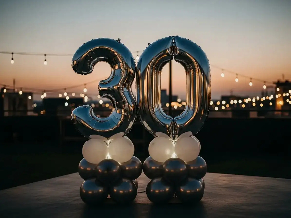 Número 30 gigante con globos metálicos plateados en escena elegante al atardecer