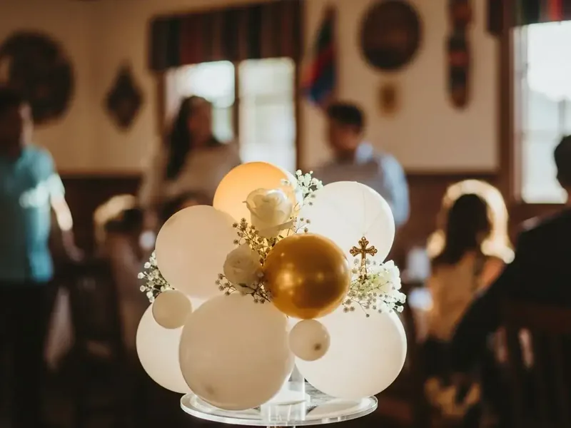 Centro de mesa de globos en blanco, crema y dorado con ramas de gypsophila, sobre una mesa de recepción