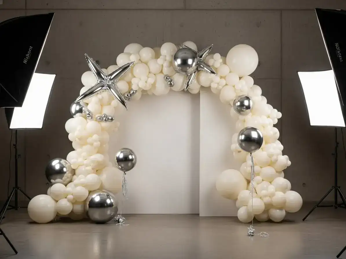 Arco de globos blanco y plateado con globos foil de estrella en sesión de fotos de estudio con fondo gris
