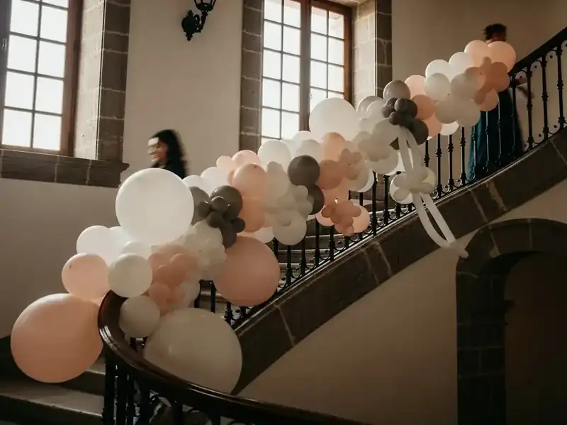 Guirnalda de globos en tonos neutros crema, durazno y gris sobre el barandal de hierro de una escalera de boda