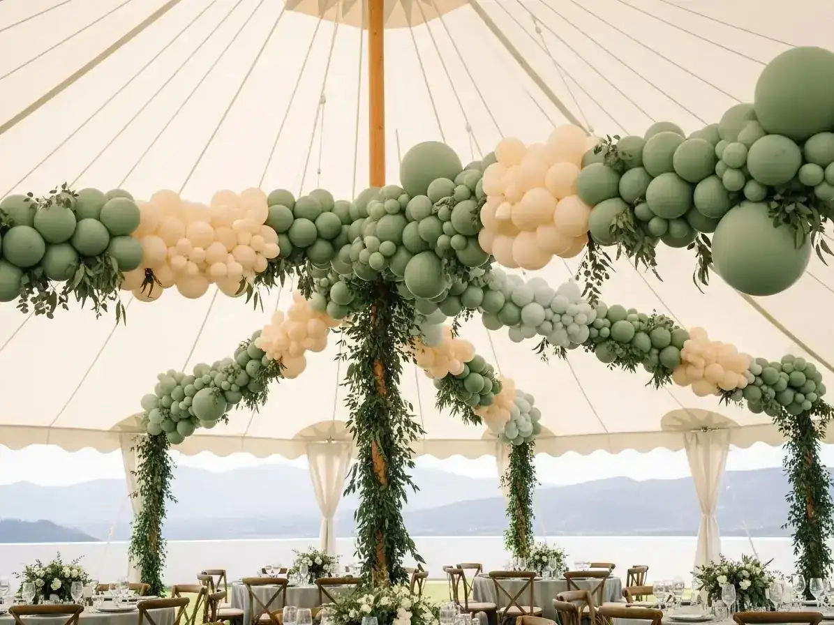 Guirnaldas de globos verde salvia cruzando el techo de una carpa de boda con vista al lago